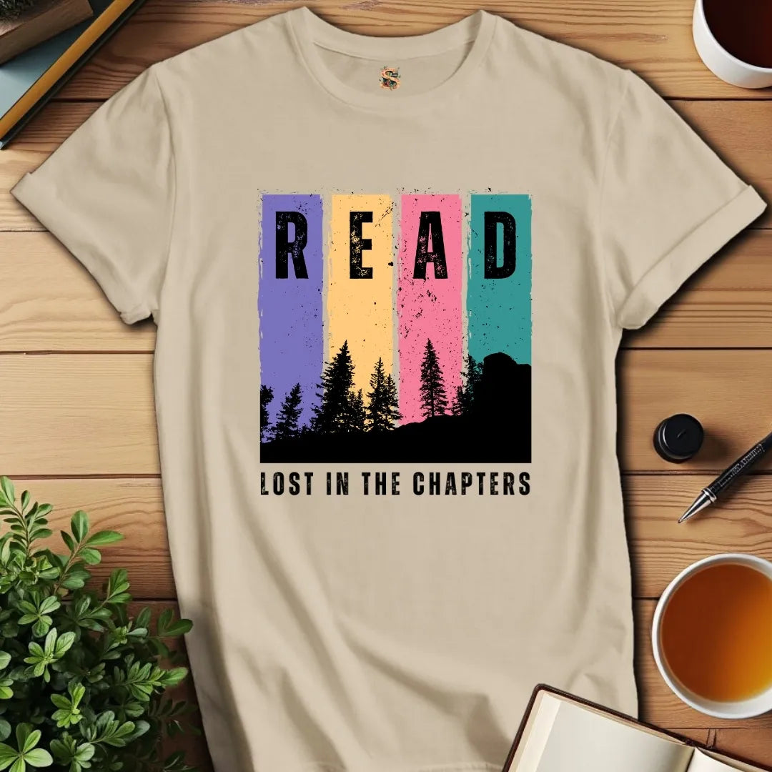 Beige t-shirt with 'READ LOST IN THE CHAPTERS' design on a wooden surface with books and a cup of tea.