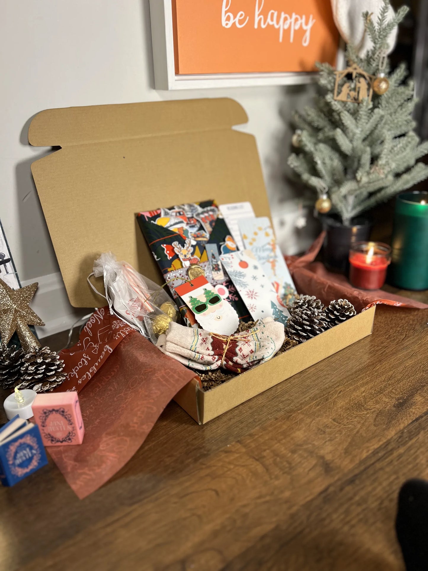 Open Blind date with a book box with Christmas-themed items on a wooden surface, with a 'be happy' sign in the background.