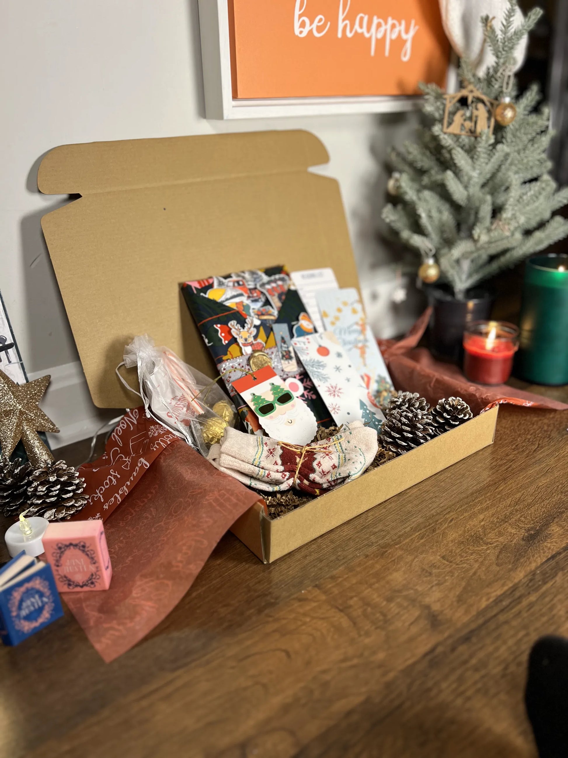 Open Blind date with a book box with Christmas-themed items on a wooden surface, with a 'be happy' sign in the background.