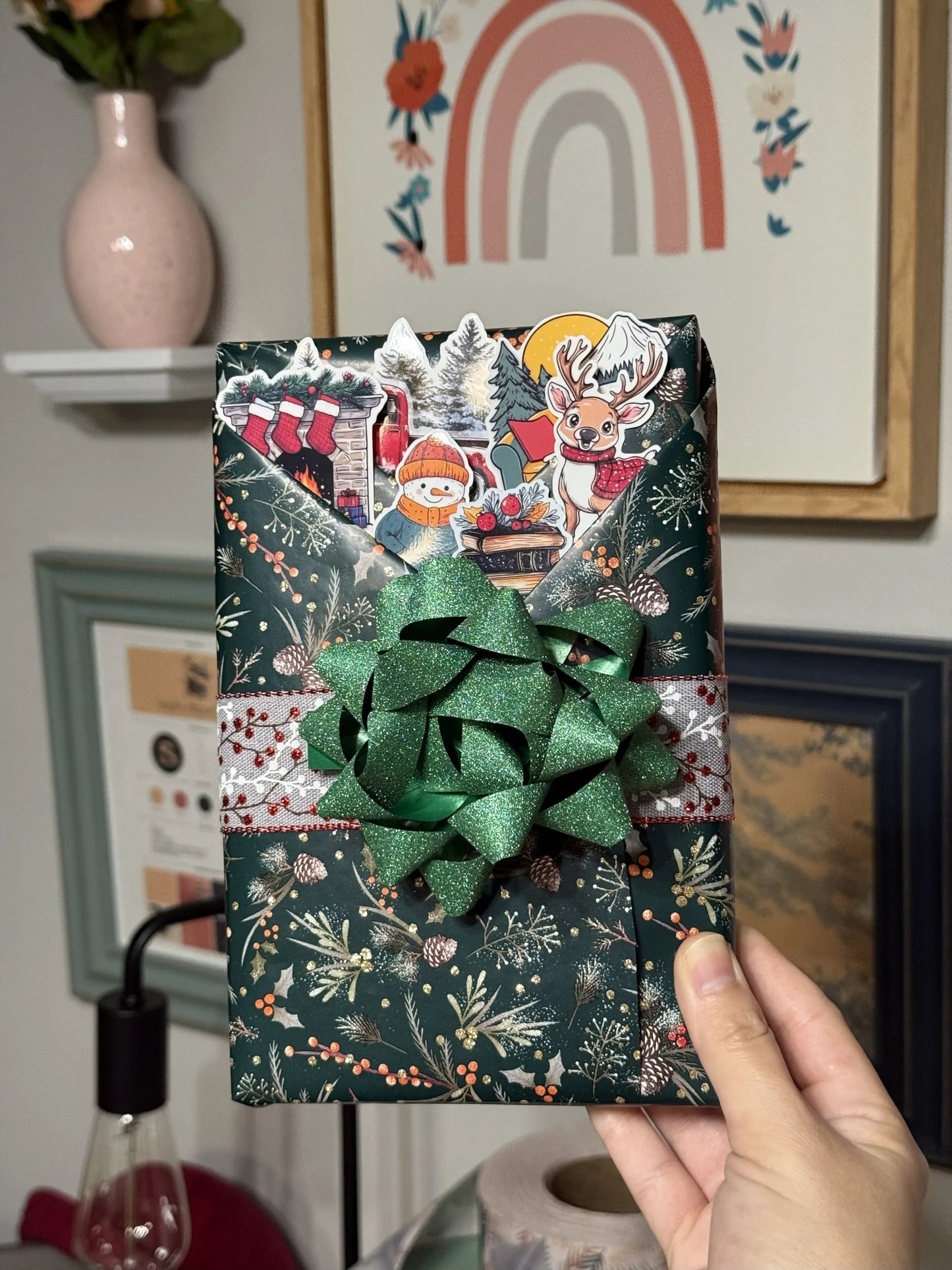 Christmas themed blind date with a book with decorative paper and green bow held in front of a wall with framed pictures.