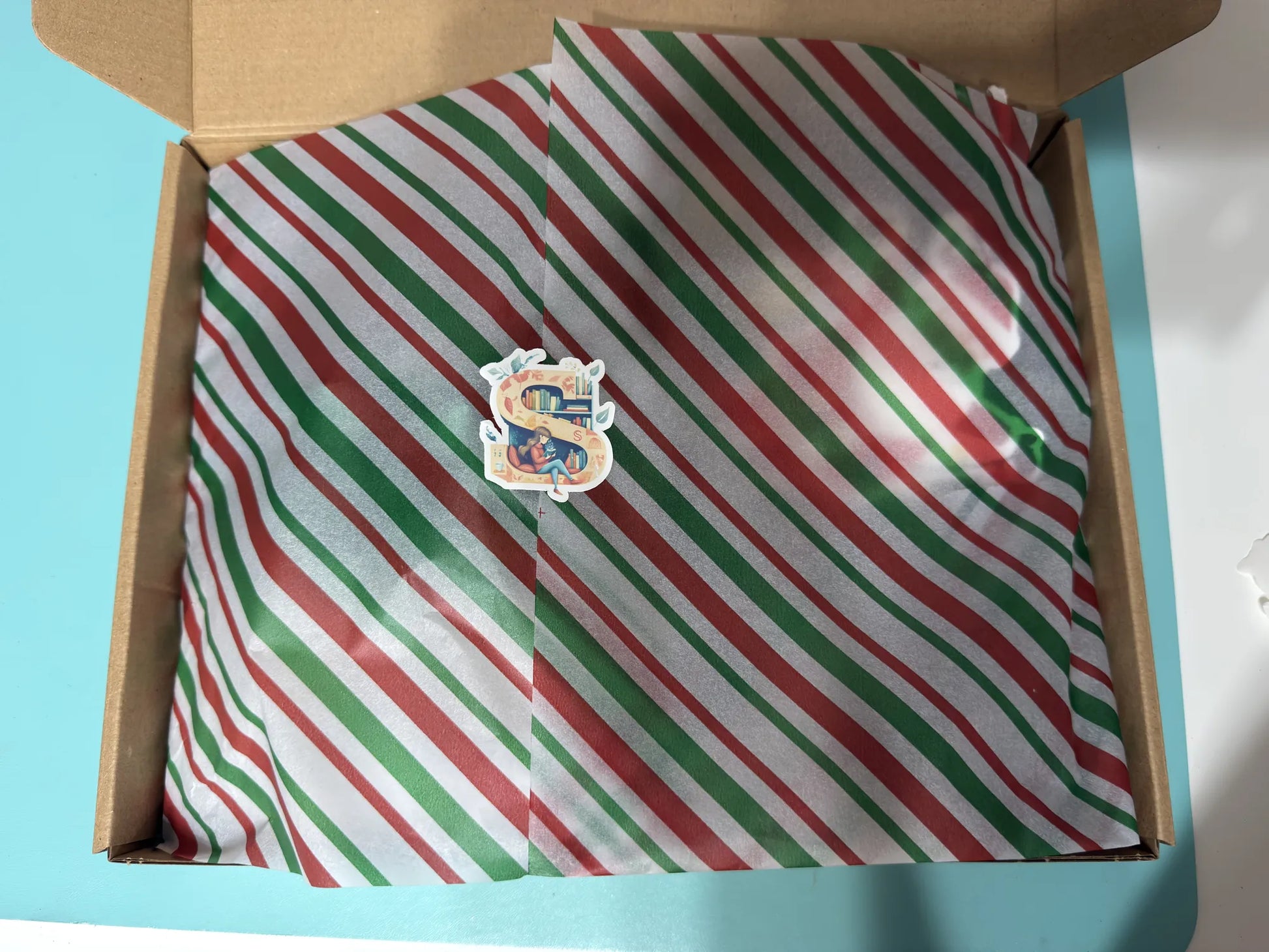 Open box with red, green, and white striped paper featuring a logo.