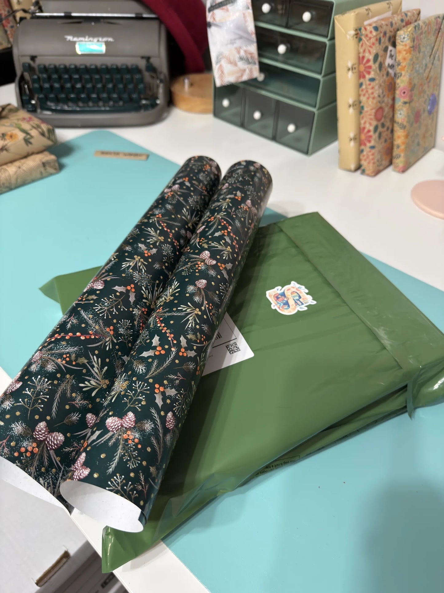 Two rolls of floral-patterned wrapping paper on a desk with a typewriter and stationery items in the background.