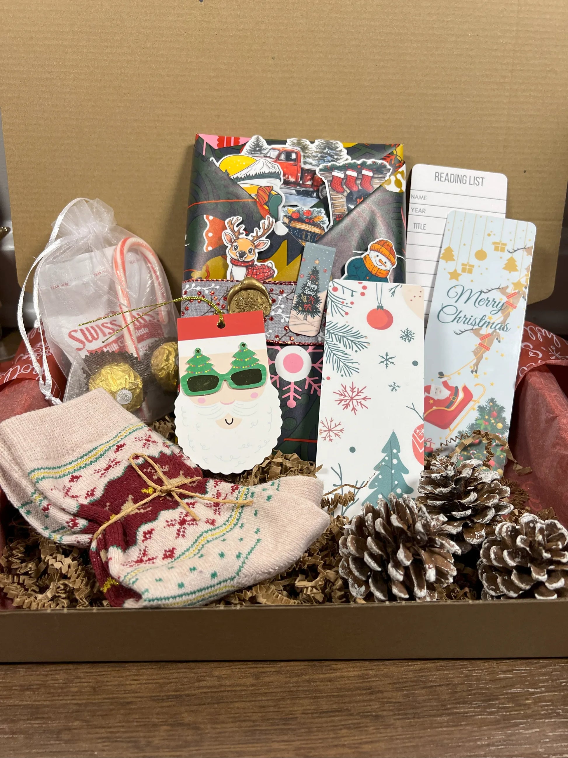 Gift box with Christmas-themed items including a book, socks, cards, and decorative elements.